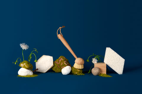 Sqwishful zero waste kitchen and home essentials: plant-powered and plastic-free pop up sponge, scrub sponge, and dish brush with stones covered in moss, rocks, wood blocks, and tiny flowers.